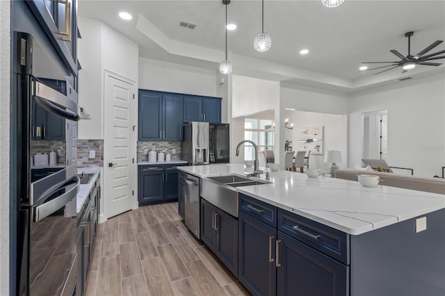 kitchen with appliances with stainless steel finishes, ceiling fan, a raised ceiling, and a kitchen island with sink