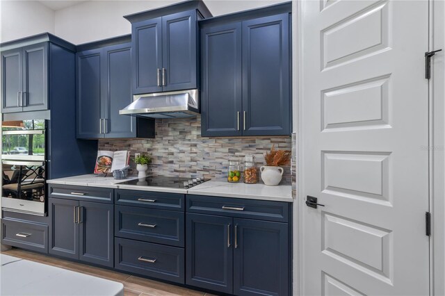 kitchen with black electric cooktop, tasteful backsplash, blue cabinets, and light stone countertops