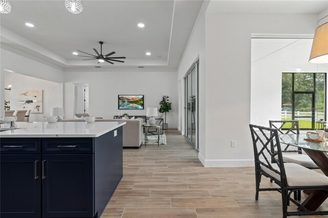 kitchen with a raised ceiling, light stone counters, and ceiling fan