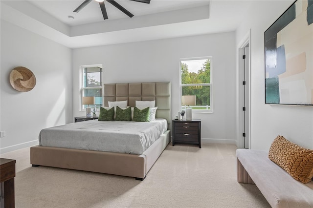 bedroom with light carpet, ceiling fan, and a raised ceiling