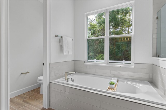 bathroom with tiled tub, toilet, and hardwood / wood-style floors