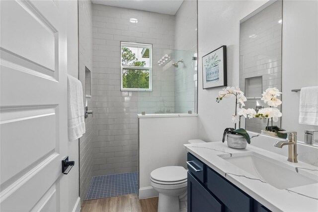 bathroom featuring toilet, hardwood / wood-style floors, vanity, and a tile shower