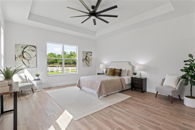 bedroom featuring light wood-type flooring, ceiling fan, and a raised ceiling