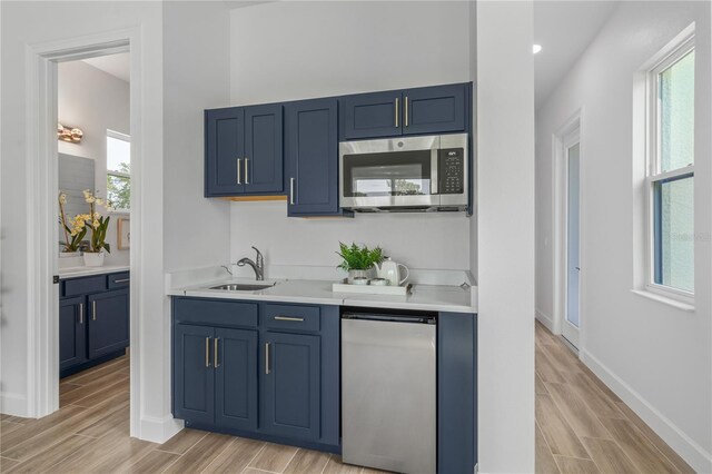 kitchen with blue cabinetry, stainless steel appliances, light hardwood / wood-style flooring, and sink