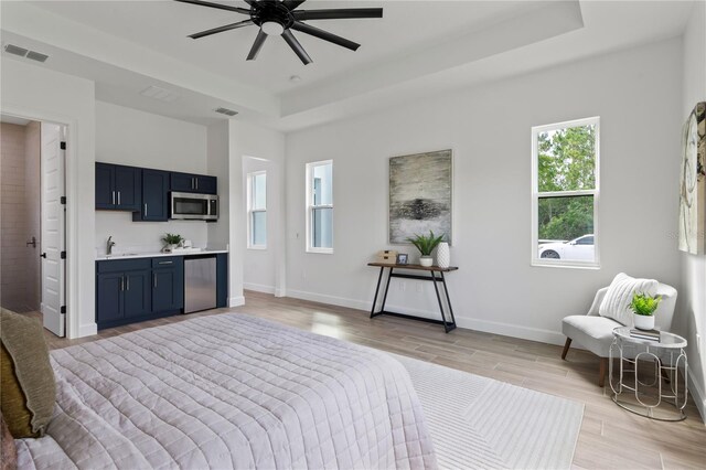 bedroom with a raised ceiling, ensuite bathroom, light wood-type flooring, and ceiling fan