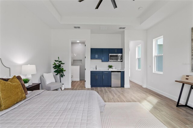 bedroom featuring a tray ceiling, light hardwood / wood-style floors, ensuite bath, and ceiling fan