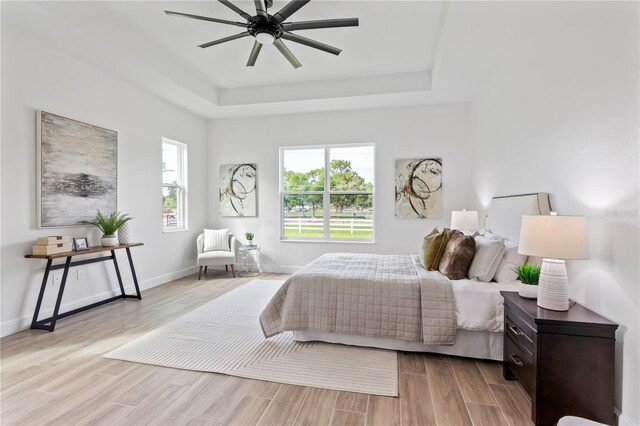 bedroom featuring light wood-type flooring, ceiling fan, and a raised ceiling