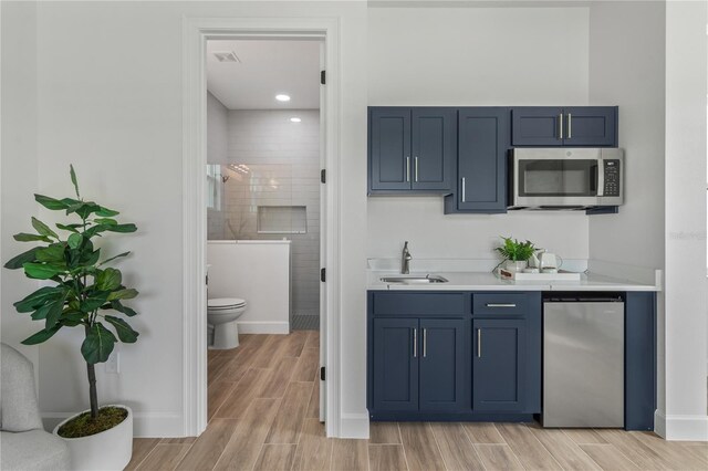 bar featuring sink, appliances with stainless steel finishes, light hardwood / wood-style flooring, and blue cabinetry