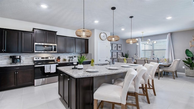 kitchen featuring light stone countertops, hanging light fixtures, a center island with sink, and stainless steel appliances