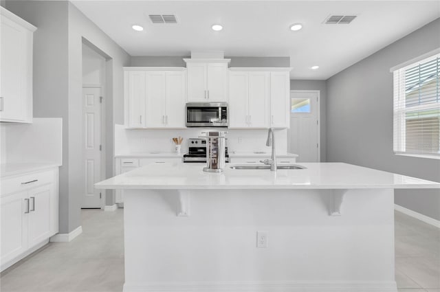 kitchen featuring appliances with stainless steel finishes, sink, white cabinetry, and a center island with sink