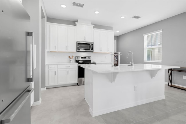 kitchen featuring white cabinets, appliances with stainless steel finishes, a breakfast bar, and an island with sink