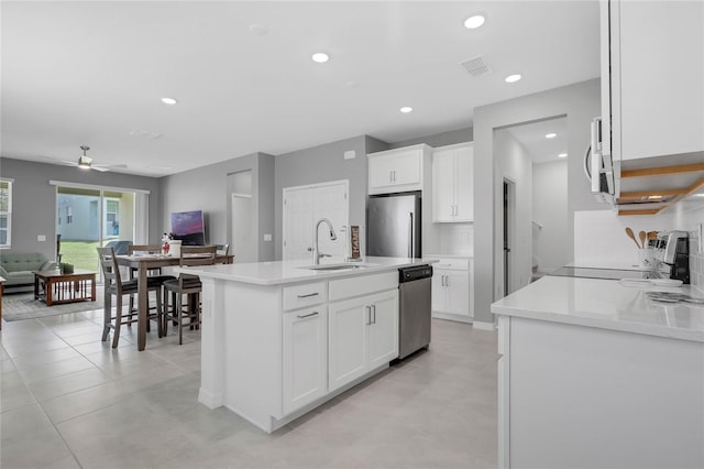 kitchen with white cabinets, stainless steel appliances, backsplash, ceiling fan, and a center island with sink