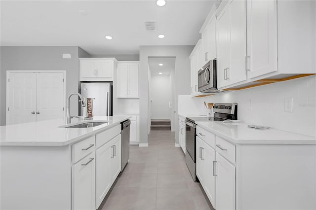 kitchen with white cabinets, appliances with stainless steel finishes, sink, light tile patterned floors, and a center island with sink