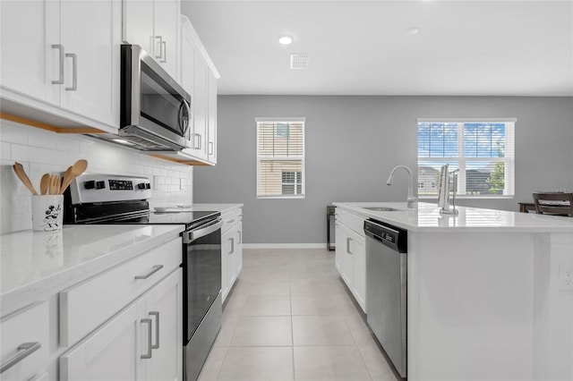 kitchen with white cabinetry, stainless steel appliances, an island with sink, sink, and backsplash