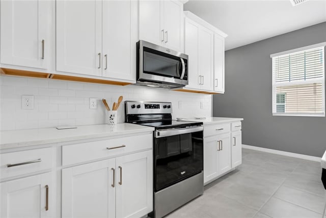 kitchen with tasteful backsplash, light tile patterned flooring, appliances with stainless steel finishes, white cabinets, and light stone counters