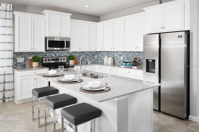 kitchen featuring a kitchen breakfast bar, stainless steel appliances, sink, white cabinetry, and an island with sink