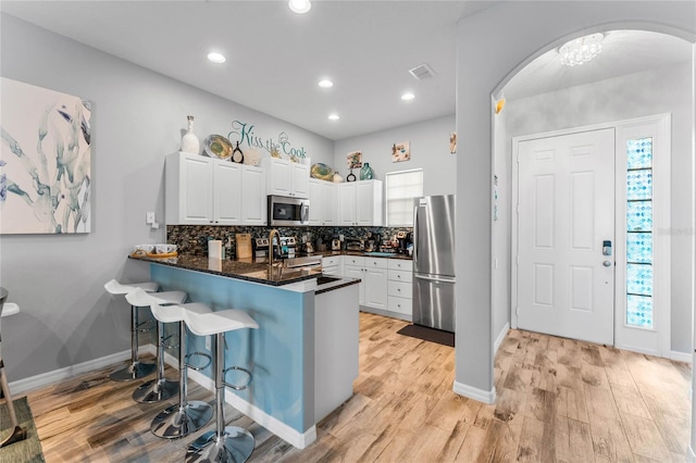 kitchen with stainless steel appliances, a wealth of natural light, white cabinets, decorative backsplash, and kitchen peninsula