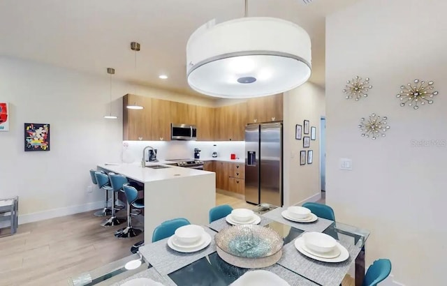 kitchen with kitchen peninsula, stainless steel appliances, light hardwood / wood-style floors, pendant lighting, and a kitchen breakfast bar