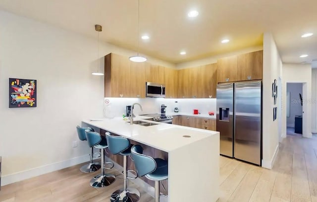 kitchen featuring decorative light fixtures, sink, appliances with stainless steel finishes, light hardwood / wood-style flooring, and a kitchen breakfast bar