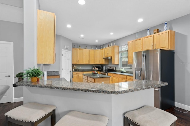 kitchen featuring dark stone countertops, a kitchen breakfast bar, kitchen peninsula, stainless steel appliances, and light brown cabinets