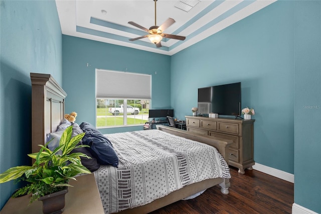 bedroom with dark wood-type flooring, ceiling fan, and a tray ceiling