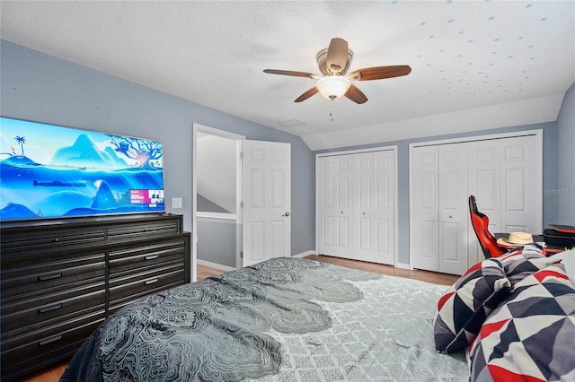 bedroom featuring ceiling fan, lofted ceiling, hardwood / wood-style floors, and two closets