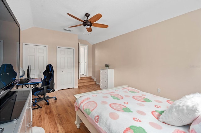 bedroom featuring ceiling fan, vaulted ceiling, light hardwood / wood-style flooring, and two closets