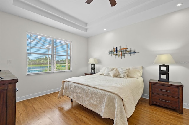 bedroom with ceiling fan, light hardwood / wood-style flooring, and a tray ceiling