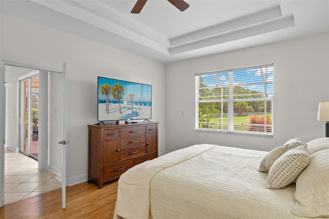 bedroom with access to exterior, light hardwood / wood-style flooring, ceiling fan, and a raised ceiling