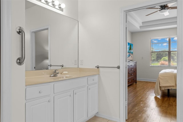 bathroom with ceiling fan, wood-type flooring, vanity, and a raised ceiling