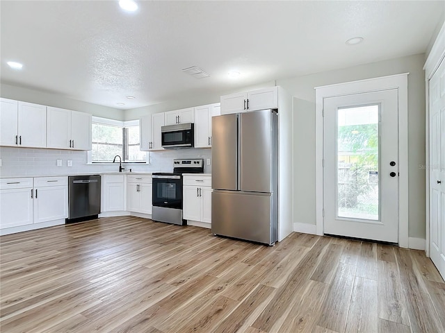 kitchen with white cabinetry, decorative backsplash, stainless steel appliances, and light wood-type flooring