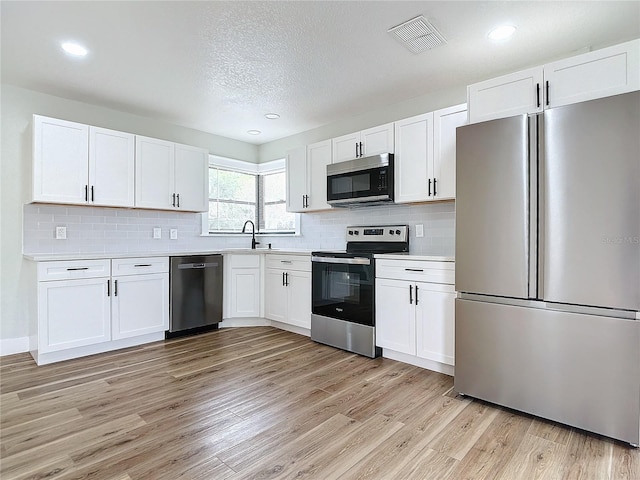 kitchen with sink, appliances with stainless steel finishes, white cabinetry, backsplash, and light hardwood / wood-style floors