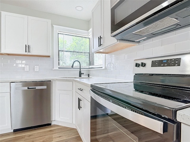 kitchen featuring appliances with stainless steel finishes, white cabinetry, sink, decorative backsplash, and light stone counters