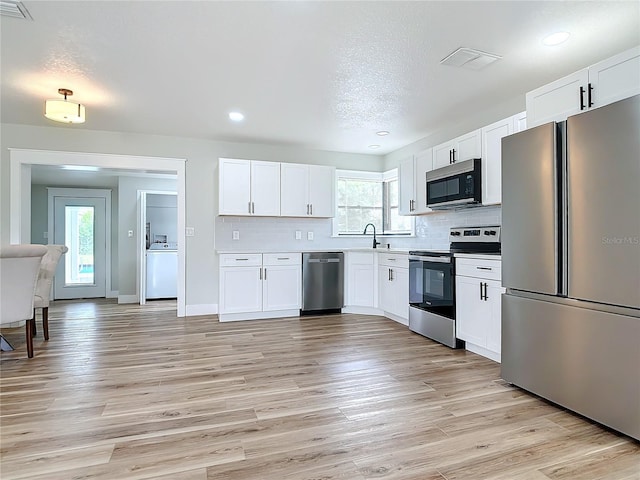 kitchen with white cabinetry, appliances with stainless steel finishes, tasteful backsplash, and light hardwood / wood-style flooring