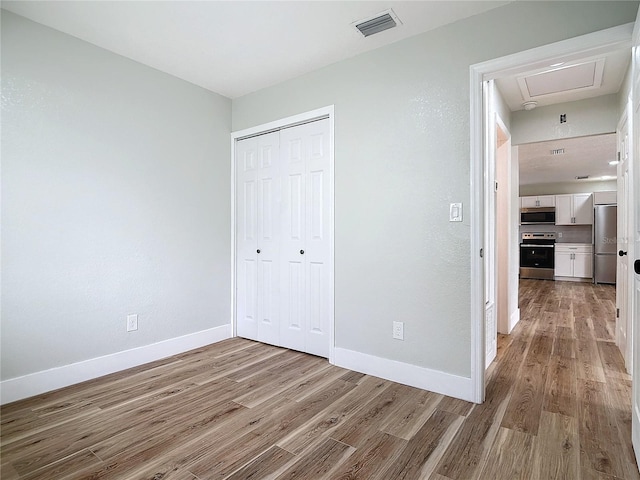 unfurnished bedroom featuring built in fridge, light hardwood / wood-style floors, and a closet