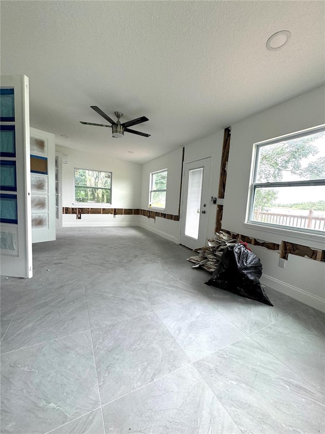 unfurnished living room featuring ceiling fan, a healthy amount of sunlight, and a textured ceiling