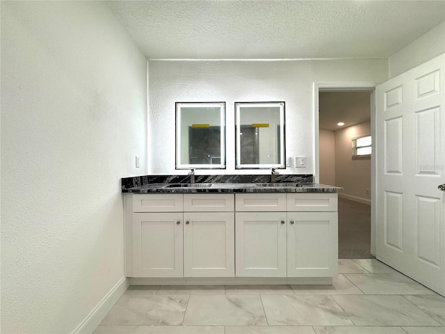 bathroom featuring a textured ceiling, marble finish floor, double vanity, and a sink