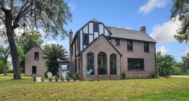 tudor house featuring stucco siding, a chimney, a front lawn, and brick siding