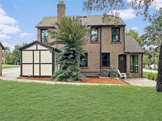 back of property with a yard, a shingled roof, a chimney, and brick siding