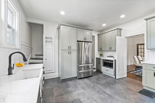 kitchen with appliances with stainless steel finishes, gray cabinetry, decorative backsplash, light stone countertops, and dark wood-type flooring