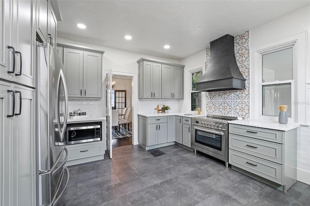 kitchen featuring decorative backsplash, stainless steel appliances, light countertops, gray cabinetry, and premium range hood