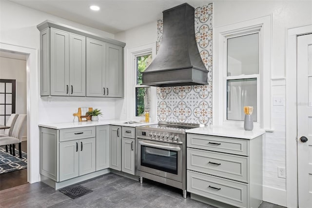 kitchen with light countertops, high end stainless steel range oven, gray cabinets, tasteful backsplash, and custom range hood