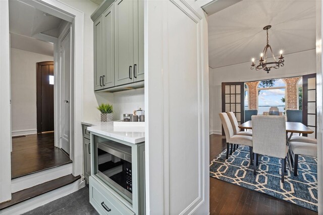 kitchen with pendant lighting, light stone counters, stainless steel microwave, dark wood-type flooring, and a notable chandelier