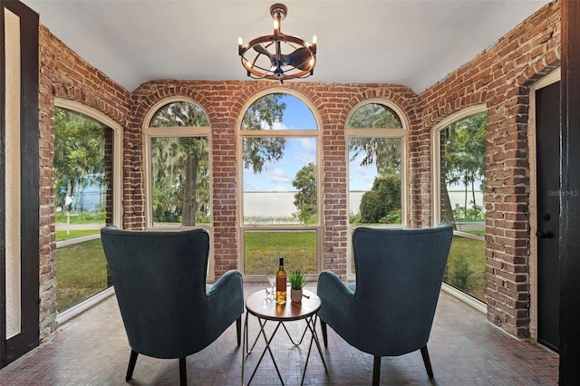 interior space featuring brick floor, brick wall, a wealth of natural light, and an inviting chandelier