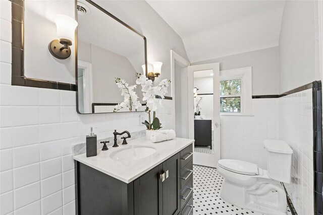 bathroom with tile patterned flooring, lofted ceiling, toilet, vanity, and tile walls