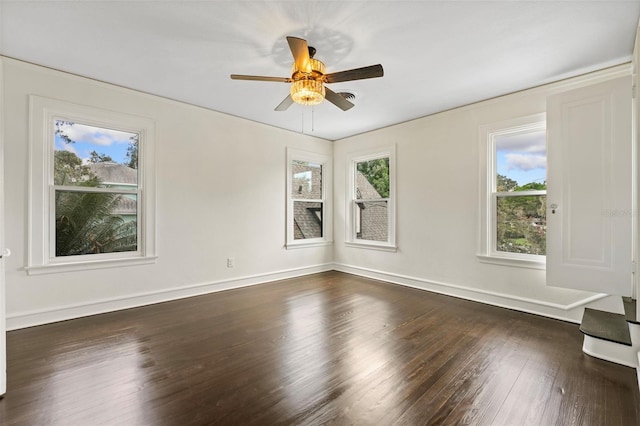 empty room with dark wood-type flooring, a wealth of natural light, ceiling fan, and baseboards