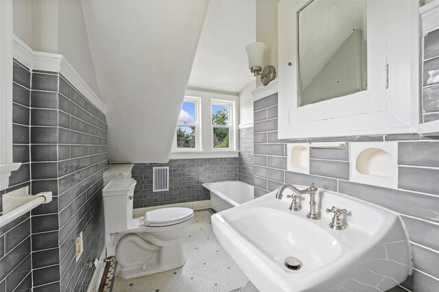 bathroom with toilet, tile patterned floors, lofted ceiling, and tile walls