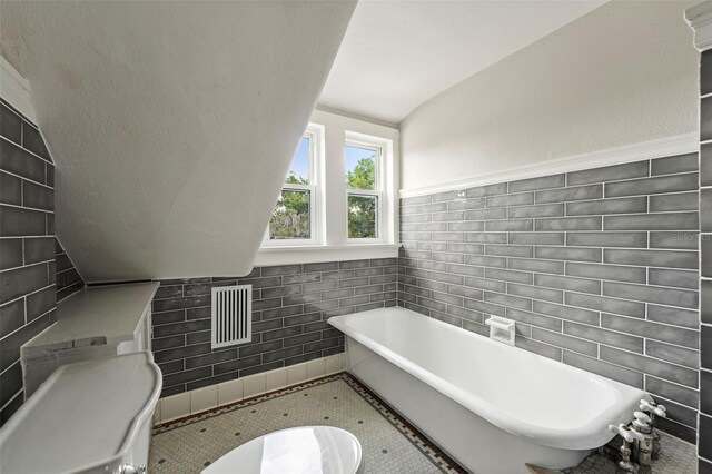 bathroom featuring vaulted ceiling, a tub to relax in, tile patterned floors, and tile walls