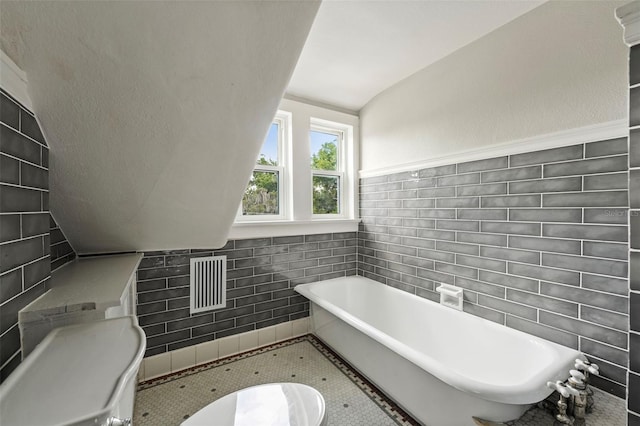 full bathroom with visible vents, a freestanding tub, tile walls, and lofted ceiling