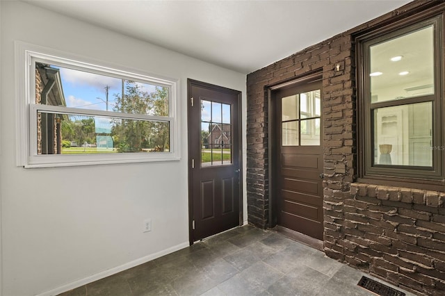 foyer entrance with brick wall and dark tile patterned flooring